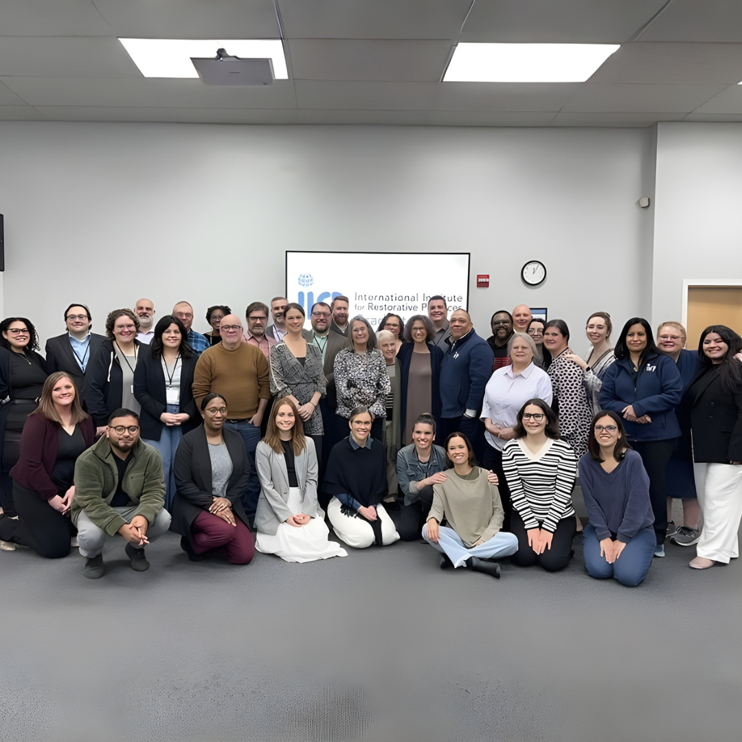 Photo of IIRP faculty and staff gathered in front of the IIRP logo.